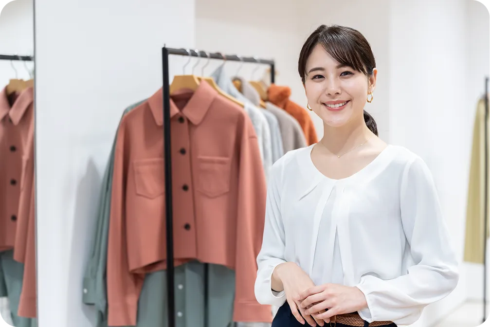 並べられた衣類の前で微笑む女性の写真